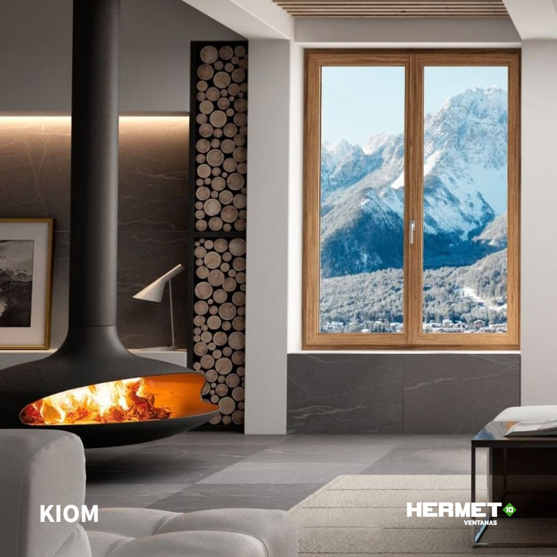 Interior moderno con chimenea y ventana de madera que muestra una vista panorámica de montañas nevadas.